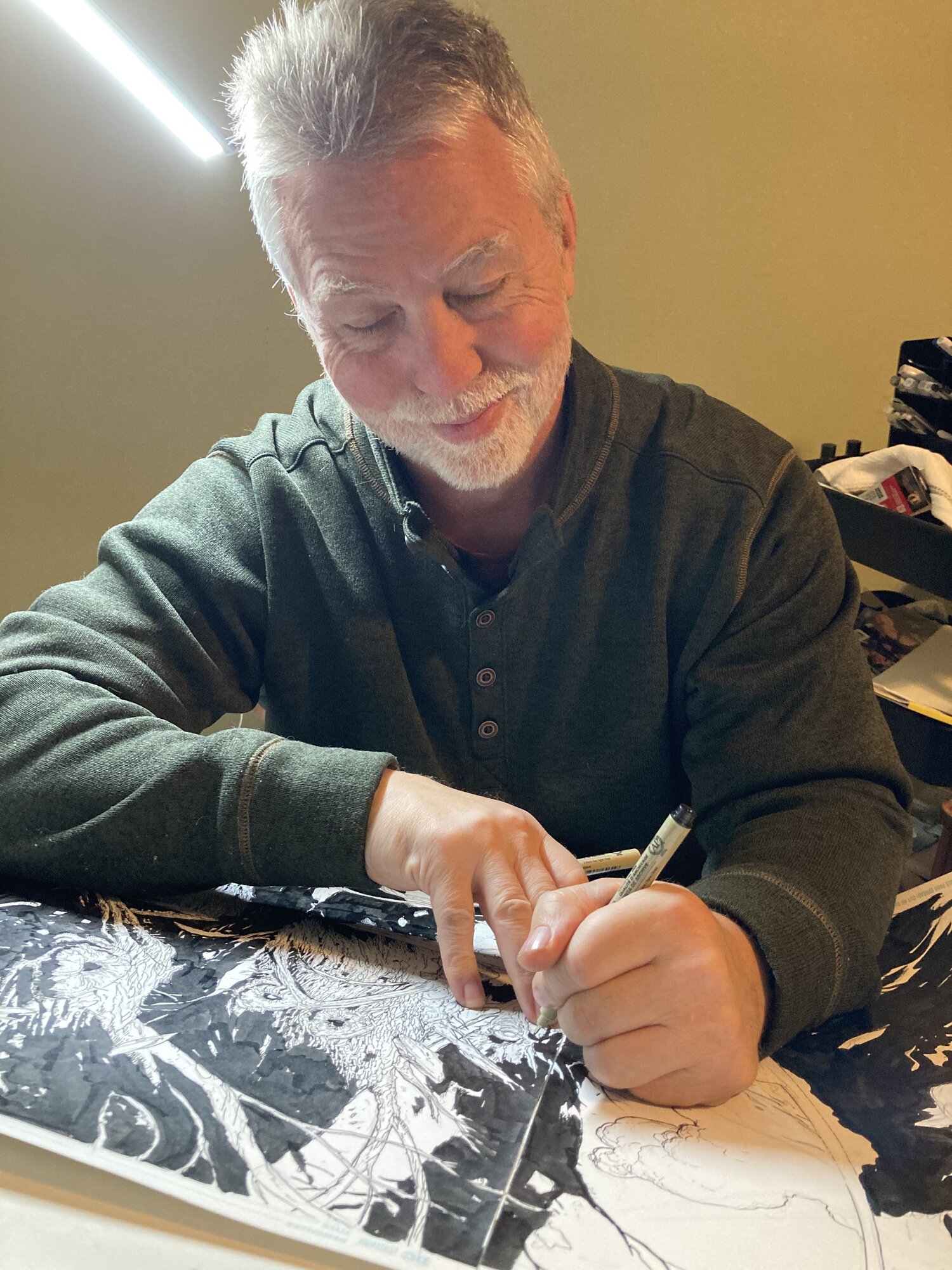 Doug Mahnke inking a creature splash page, glancing up from the board