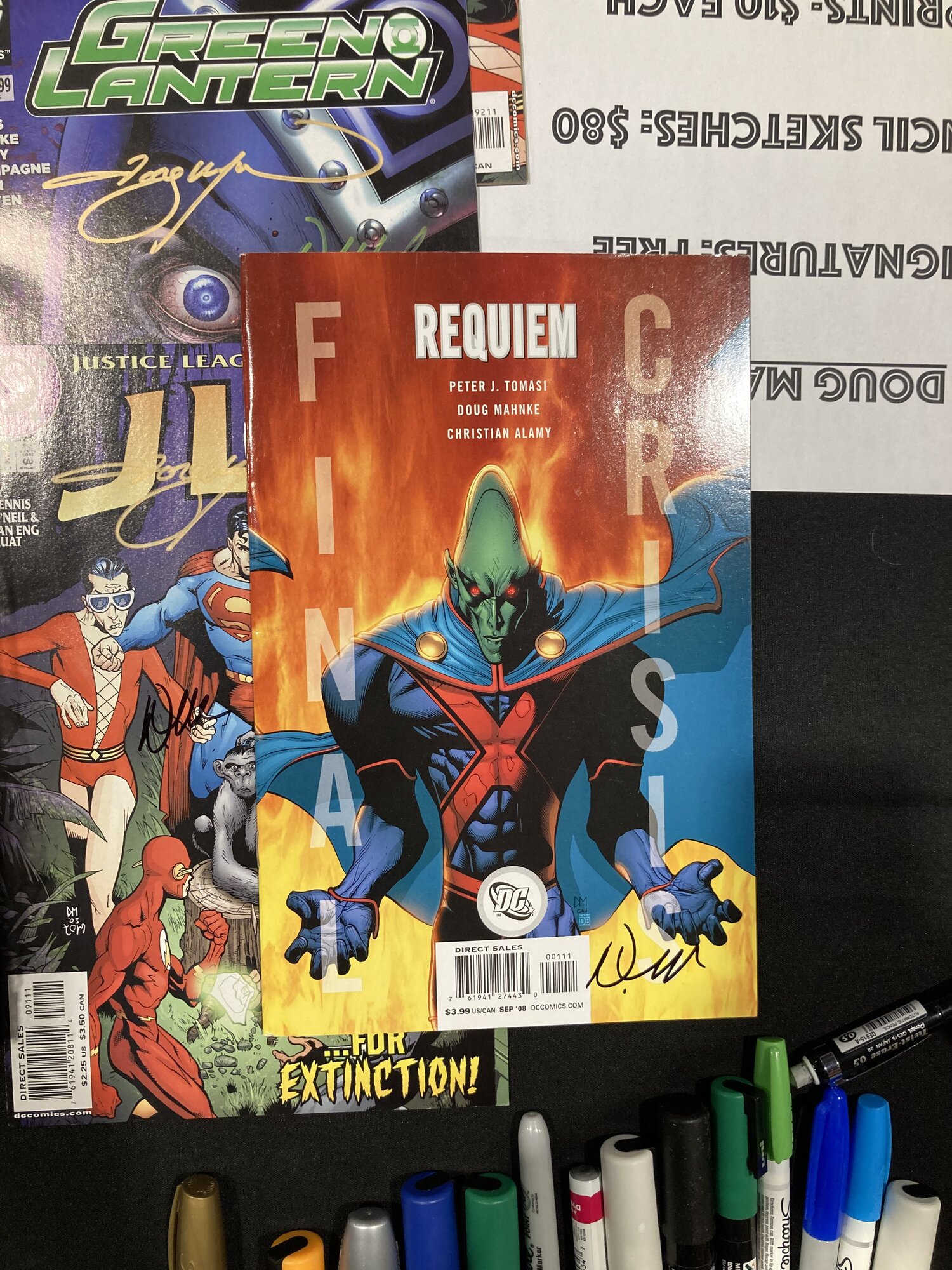 Signed comics from Final Crisis, JLA and Green Lantern stacked on a convention table